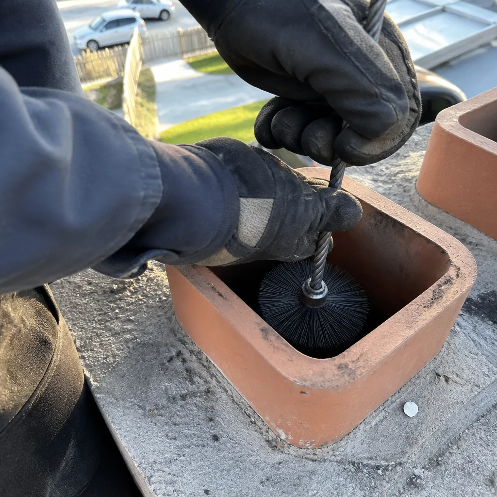 Professional chimney sweep cleaning a brick chimney flue with a wire brush